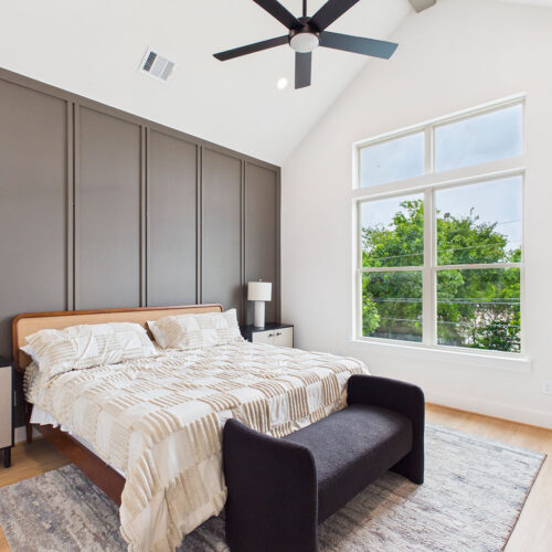 Spacious primary bedroom with vaulted ceiling, designer accent wall, large windows, and modern finishes in Houston luxury home.