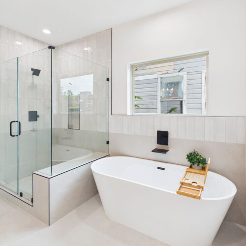 Luxury primary bathroom with freestanding soaking tub, glass-enclosed shower, designer tile, and modern black fixtures.