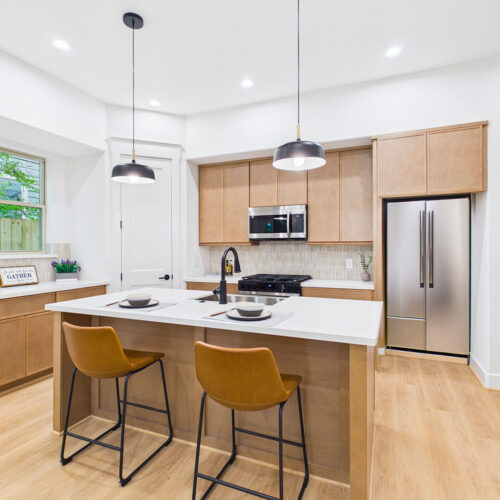 Designer kitchen with oversized quartz island, custom cabinetry, stainless steel appliances, and breakfast seating in Houston new construction home.