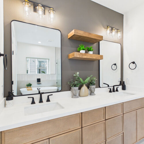 Luxury primary bathroom with dual vanity, quartz countertops, black fixtures, floating wood shelves, and custom accent wall.