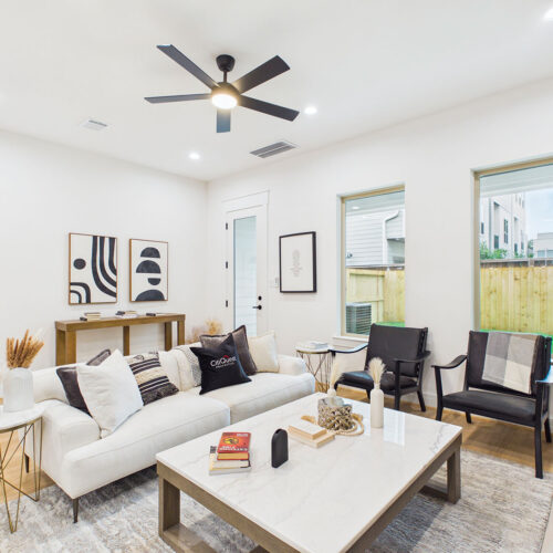Open-concept living room with modern furnishings, large windows, and backyard views in Houston new construction home.
