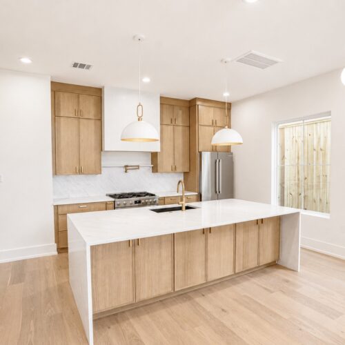 Luxury kitchen in The Heights Houston featuring a waterfall quartz island, custom wood cabinetry, designer lighting, and open-concept living.
