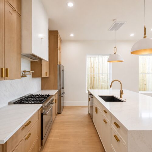 Luxury chef’s kitchen in The Heights Houston featuring a waterfall quartz island, custom wood cabinetry, gas range, and designer brass fixtures.