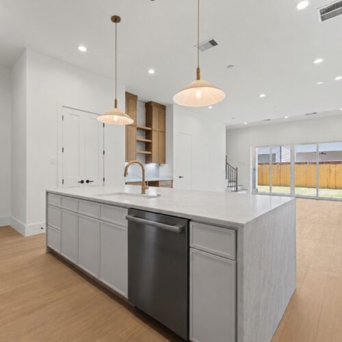 Luxury open-concept kitchen in The Heights Houston featuring an oversized quartz island, designer lighting, and backyard views.