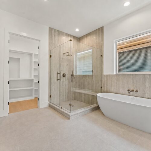 Luxury primary bathroom in The Heights Houston featuring a freestanding soaking tub, walk-in glass shower, custom tile, and designer brass fixtures.